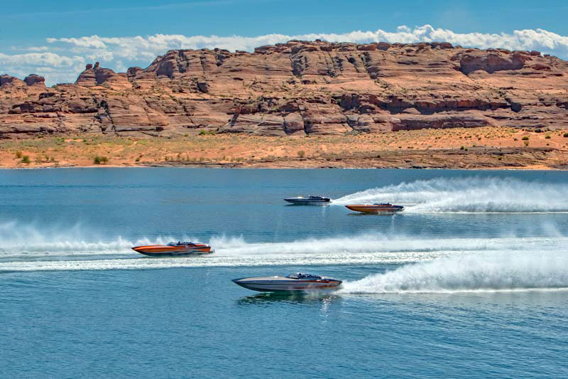 Four speedboats racing across blue water with red rock cliffs in the background, capturing an energetic, sporty mood.